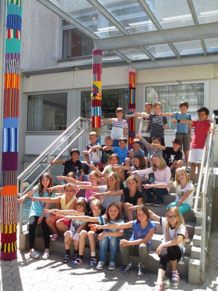 Stolz zeigen die Kinder auf ihr kunterbuntes Werk: Die Säulen am Eingang der Grundschule wurden umhäkelt.