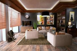 Wohnzimmer mit moderner Couchgarnitur, Holzregalen, Kunstwerken an der Wand und einem TV-Schrank. Der Raum hat Holzboden und große Fenster mit Holzjalousien.