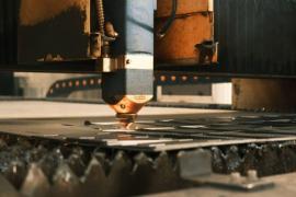 Ein Laser-Schneidkopf einer industriellen CNC-Laserschneidanlage bearbeitet eine Metallplatte.