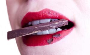 Nahaufname eines Frauenmunds mit rotem Lippenstift und Schokolade im Mund