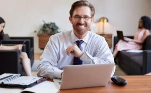 Ein Mann in Businesskleidung sitzt an einem Schreibtisch mit seinem Laptop.