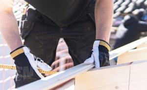 Ein Bauarbeiter mit Handschuhen misst Holz auf einer Baustelle.
