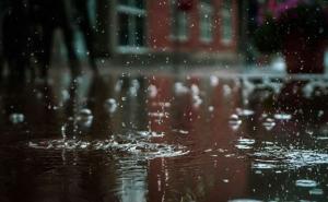 Regentropfen fallen auf eine regennasse Straße vor einem Gebäude.