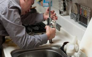 Ein Mann steht in der Küche und repariert den Wasserhahn am Spülbecken.