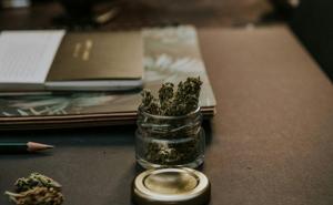 Notizbuch und Glas mit Cannabis auf einem Schreibtisch