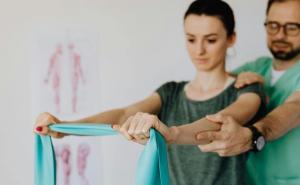 Eine Frau macht unter Anleitung eines Physiotherapeuten eine Übung mit einem Widerstandsband.
