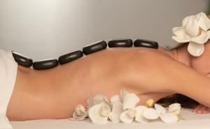 Eine Frau mit Hot-Stone-Massagesteinen auf dem Rücken und weißen Blüten daneben