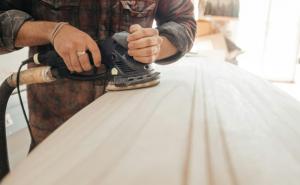 Ein Mann schleift ein Holzbrett mit einer Schleifmaschine.