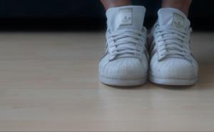 Weiße Sportschuhe an den Füßen einer Person auf hellem Holzboden