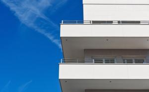 Modernes weißes Gebäude mit mehreren Balkonen vor einem blauen Himmel