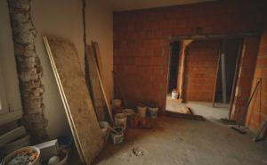 Baustelle im Innenraum mit rohen Ziegelwänden, Baumaterialien und offenem Durchgang.