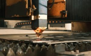 Ein Laser-Schneidkopf einer industriellen CNC-Laserschneidanlage bearbeitet eine Metallplatte.