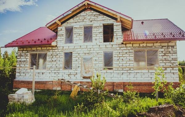 Einfamilienhaus im Rohbau mit roten Dachziegeln, unverputzten Betonwänden und modernen Bauelementen für Fenster und Türen