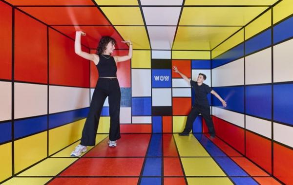 Ein Mann und eine Frau stehen in einem farbenfrohen Raum, der mit lebhaften Farben und kreativen Elementen gestaltet ist.  