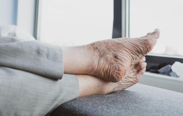 Die Füße einer älteren Person ruhen auf einer gepolsterten Fläche.