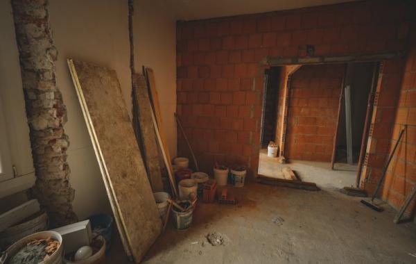 Baustelle im Innenraum mit rohen Ziegelwänden, Baumaterialien und offenem Durchgang.