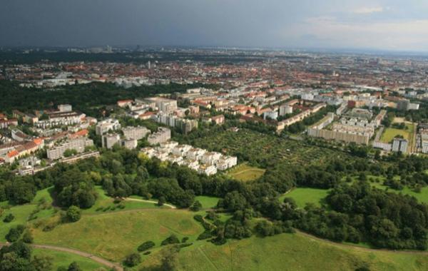 Luftaufnahme einer Stadt mit dicht bebauten Wohnhäusern und einer grünen Landschaft im Vordergrund