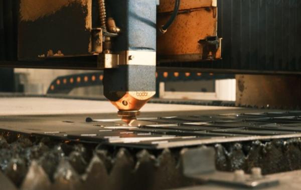 Ein Laser-Schneidkopf einer industriellen CNC-Laserschneidanlage bearbeitet eine Metallplatte.