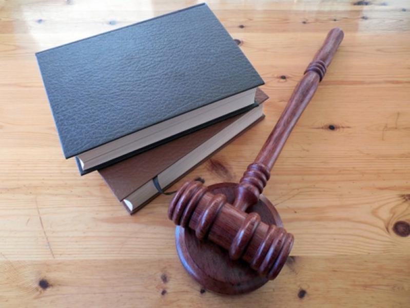Auf einem Holztisch befinden sich ein Richterhammer und mehrere Bücher, die das Thema Recht und Justiz repräsentieren.