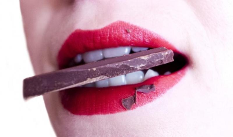 Nahaufname eines Frauenmunds mit rotem Lippenstift und Schokolade im Mund