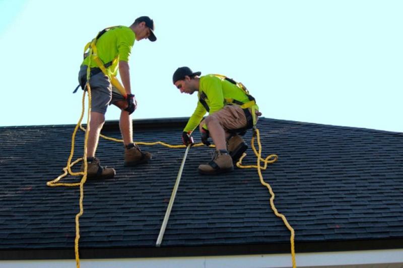 Zwei Männer, die mit Seilen gesichert sind, arbeiten auf einem Dach.