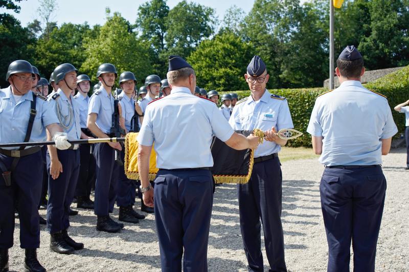Der Kommandeur der Offizierschule, Brigadegeneral Gero von Fritschen (l.) und Oberstleutnant Andreas Seebörger als bisheriger Lehrgruppenkommandeur rollen gemeinsam die Truppenfahne der II. Lehrgruppe der OSLw in einem feierlichen Akt ein und verhüllen sie anschließend mit einem schwarzen Stoffsack.