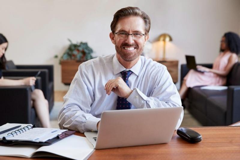 Ein Mann in Businesskleidung sitzt an einem Schreibtisch mit seinem Laptop.