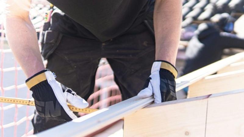 Ein Bauarbeiter mit Handschuhen misst Holz auf einer Baustelle.
