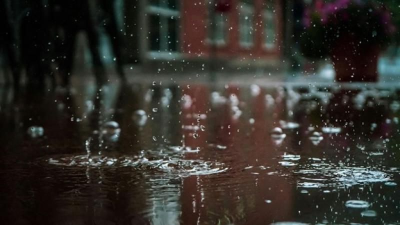 Regentropfen fallen auf eine regennasse Straße vor einem Gebäude.