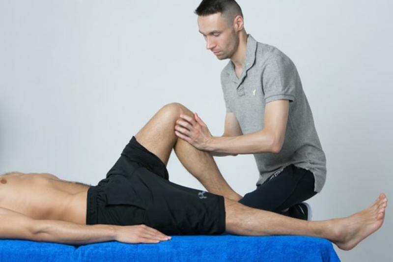Ein Physiotherapeut untersucht das Knie eines liegenden Patienten.
