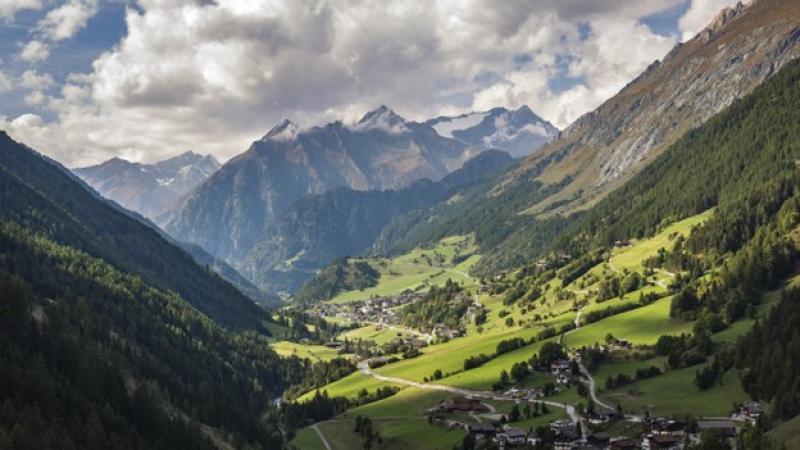 Panoramablick auf eine Gebirgslandschaft mit mit schneebedeckten Gipfeln und grünen Tälern