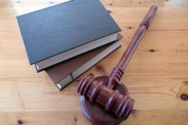 Auf einem Holztisch befinden sich ein Richterhammer und mehrere Bücher, die das Thema Recht und Justiz repräsentieren.