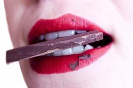 Nahaufname eines Frauenmunds mit rotem Lippenstift und Schokolade im Mund