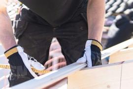 Ein Bauarbeiter mit Handschuhen misst Holz auf einer Baustelle.