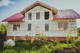Einfamilienhaus im Rohbau mit roten Dachziegeln, unverputzten Betonwänden und modernen Bauelementen für Fenster und Türen