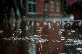 Regentropfen fallen auf eine regennasse Straße vor einem Gebäude.