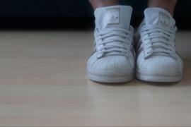 Weiße Sportschuhe an den Füßen einer Person auf hellem Holzboden