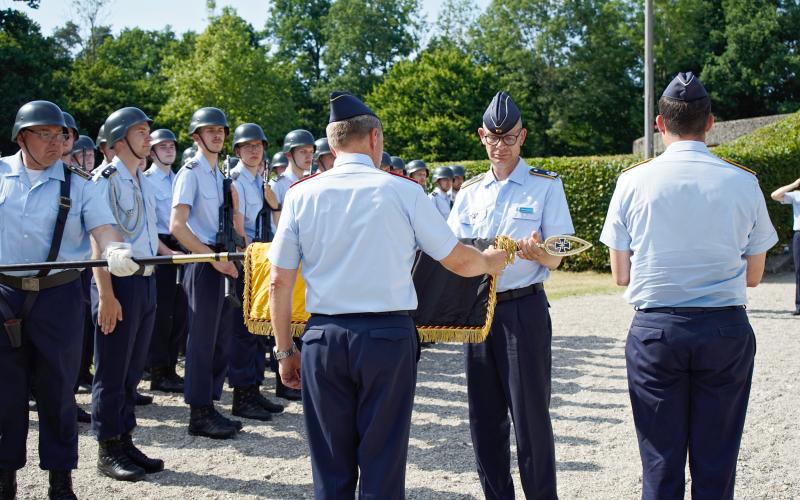 Der Kommandeur der Offizierschule, Brigadegeneral Gero von Fritschen (l.) und Oberstleutnant Andreas Seebörger als bisheriger Lehrgruppenkommandeur rollen gemeinsam die Truppenfahne der II. Lehrgruppe der OSLw in einem feierlichen Akt ein und verhüllen sie anschließend mit einem schwarzen Stoffsack.