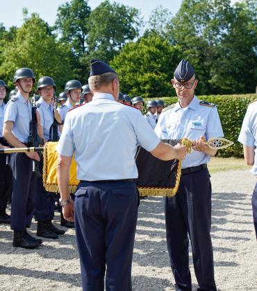 Der Kommandeur der Offizierschule, Brigadegeneral Gero von Fritschen (l.) und Oberstleutnant Andreas Seebörger als bisheriger Lehrgruppenkommandeur rollen gemeinsam die Truppenfahne der II. Lehrgruppe der OSLw in einem feierlichen Akt ein und verhüllen sie anschließend mit einem schwarzen Stoffsack.