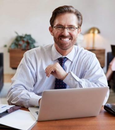 Ein Mann in Businesskleidung sitzt an einem Schreibtisch mit seinem Laptop.