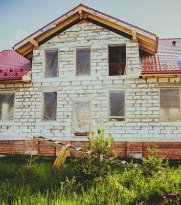Einfamilienhaus im Rohbau mit roten Dachziegeln, unverputzten Betonwänden und modernen Bauelementen für Fenster und Türen