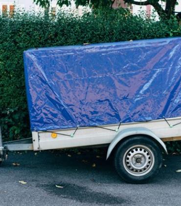 Anhänger mit blauer Plane vor einer Hecke