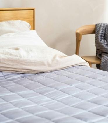 Bett mit einer gesteppten Tagesdecke und einem Stuhl daneben