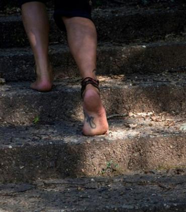 Eine Barfüßige Person geht eine steinerne Treppe im Freien hinauf.