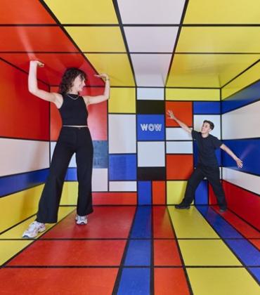 Ein Mann und eine Frau stehen in einem farbenfrohen Raum, der mit lebhaften Farben und kreativen Elementen gestaltet ist.  