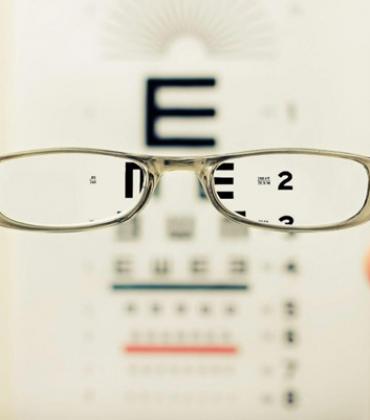 Eine Person hält eine Brille vor einen Sehtest.  