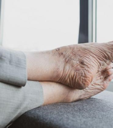 Die Füße einer älteren Person ruhen auf einer gepolsterten Fläche.