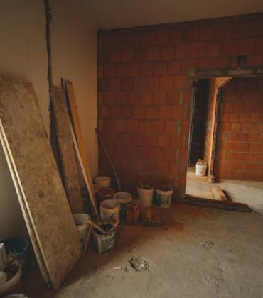 Baustelle im Innenraum mit rohen Ziegelwänden, Baumaterialien und offenem Durchgang.