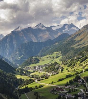 Panoramablick auf eine Gebirgslandschaft mit mit schneebedeckten Gipfeln und grünen Tälern