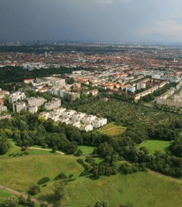 Luftaufnahme einer Stadt mit dicht bebauten Wohnhäusern und einer grünen Landschaft im Vordergrund